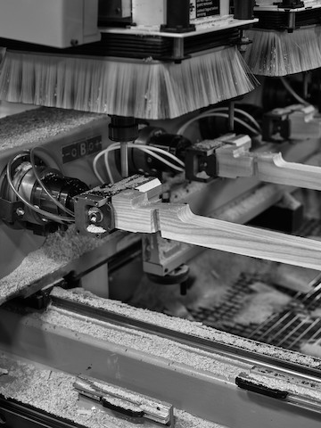 A black and white photograph of automatic milling machines carving wooden furniture parts.