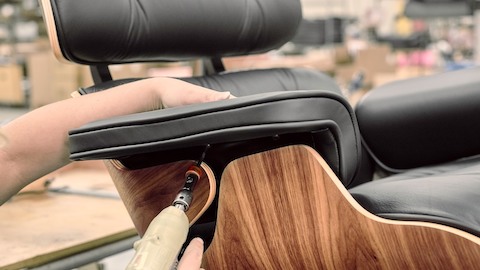A worker attaches a black leather armpad to an Eames Lounge Chair with dark walnut shell.