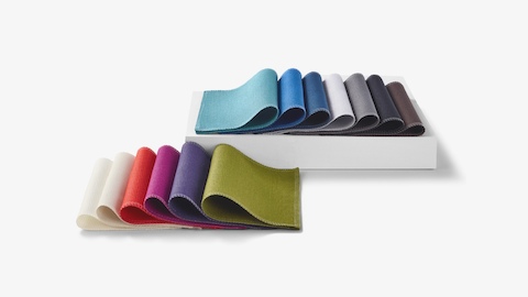 Two sets of folded, multicolor materials swatches laid out in rows with the back row elevated on a white box.