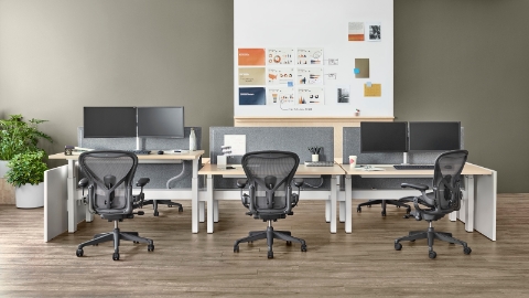 Three sit-to-stand desks in a benching configuration, each with a black Aeron office chair.