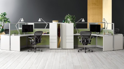 action Office estaciones de trabajo de 120 grados con monitores, iluminación de tareas, almacenamiento de taquillas y sillas de escritorio ergonómicas Aeron negras.