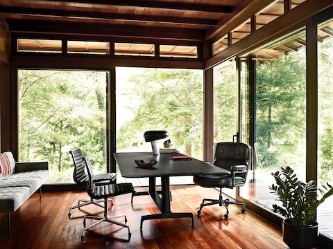 A black AGL table used as a desk in a glass-walled home office with a view of trees outside.