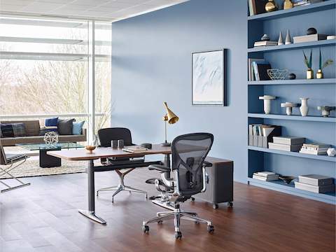A black Aeron office chair paired with an Atlas Office Landscape desk in a private office with lounge seating and a window wall.