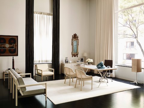 An upscale home office featuring large windows, a Brabo sofa and chair, a Nelson X-Leg Table, and a Nelson Miniature Chest.