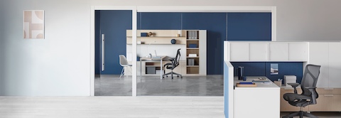 Una estación de trabajo Canvas Wall con paneles azules y almacenamiento superior blanco y un esquema Canvas Private Office en segundo plano.