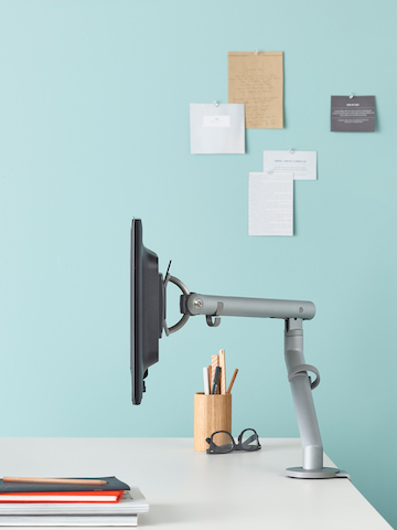 Profile view of a Flo Monitor Arm mounted on a white desk. Select to go to our technology support pages.