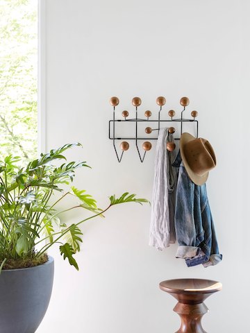 A hat and other clothing articles hang from an Eames Hang-It-All coat rack. Select to go to our decor pages.