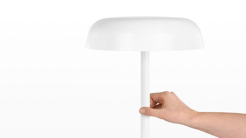 A hand touches the stem of a white Ode Lamp to turn it on or off. Select to go to our lighting pages.