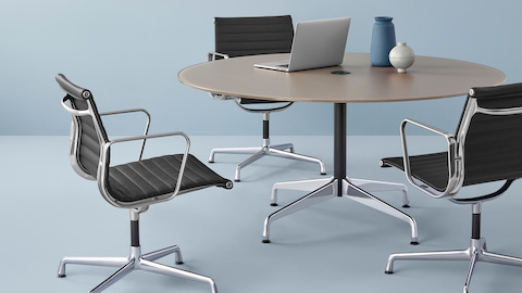 Una mesa redonda de Eames rodeada por tres Eames Aluminum Group Chairs. Seleccione para ir a la página del producto Tablas de Eames.