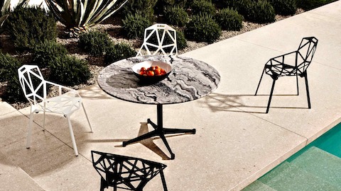 Overhead view of a stone-top Eames outdoor table next to a pool. Select to go to our outdoor tables pages.