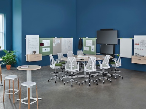 Sillas para oficinas Sayl alrededor de una mesa Exclave en forma de lágrima en un espacio de colaboración con pieza para medios colgante de pared y placas para visualización.