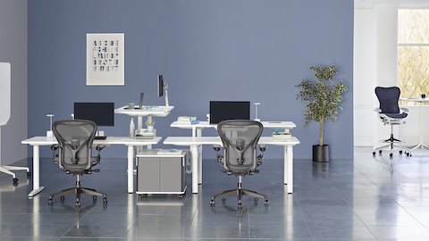 A collaboration area featuring white height-adjustable Atlas Office Landscape desks and black Aeron office chairs. Select to go to our sit-to-stand page. 