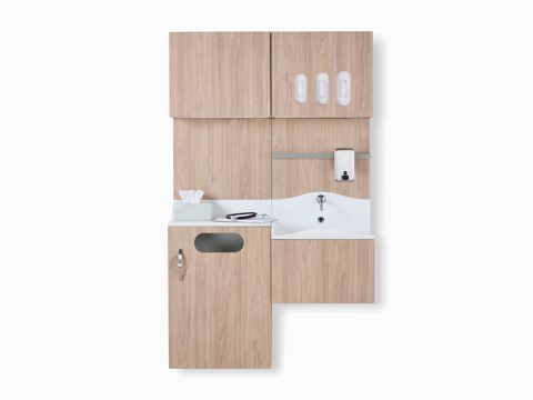 Front view of Compass System casework wall unit in a medium elm wood laminate finish with integrated waste receptacle, white solid surface sink, and upper storage for gloves.