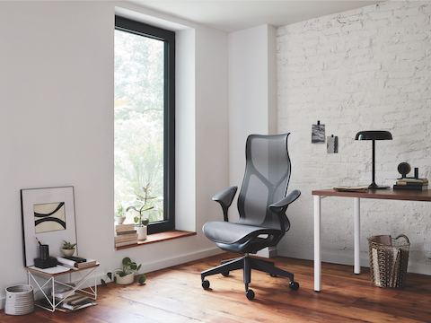 A small office with a Graphite gray Cosm high-back chair next to a rectangular Everywhere table with a walnut top and white legs.