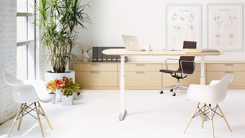 Pequeña oficina con una silla Eames Aluminum Group negra, una mesa de escritorio Renew Sit-to-Stand y dos sillas de plástico moldeadas Eames de color blanco.