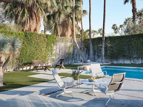 White Eames Aluminum Group outdoor chairs near a swimming pool. 