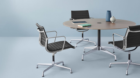 Tres sillas negras Eames Aluminum Group en medio del respaldo rodean una mesa redonda de Eames.
