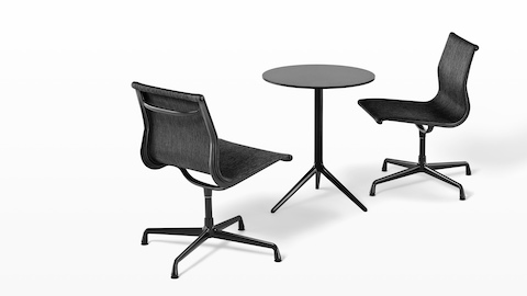 Two armless Eames Aluminum Group outdoor side chairs in a black weave fabric paired with a round black table.