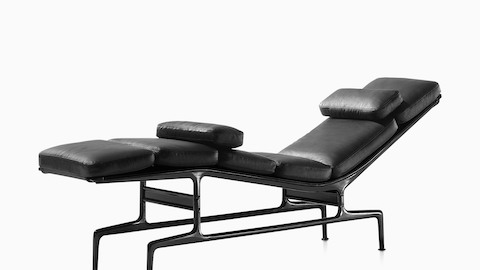 Oblique view of a black leather Eames Chaise with a black frame and two additional loose cushions.
