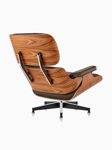 Vista trasera de tres cuartos de una silla de salón Eames de cuero marrón con una carcasa de chapa de madera.