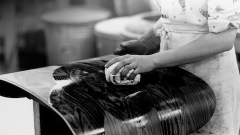 Close view of a hand applying the finish to the shell of an Eames Lounge Chair. 