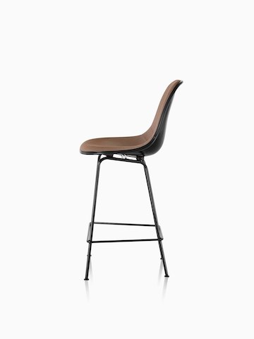 Profile view of a black Eames Molded Fiberglass Stool with brown upholstery. 
