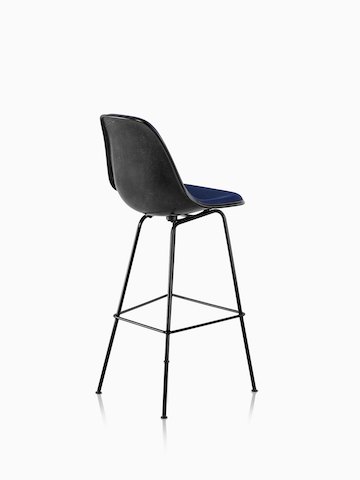 Three-quarter rear view of a black Eames Molded Fiberglass Stool with blue upholstery.