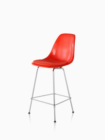Taburete de fibra de vidrio moldeado rojo Eames con un cojín de asiento rojo, visto desde un ángulo de 45 grados.
