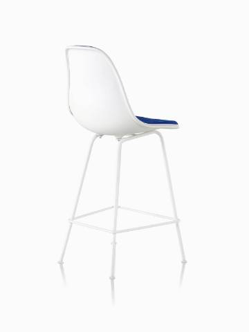 Three-quarter rear view of a white Eames Molded Plastic Stool with blue upholstery. 
