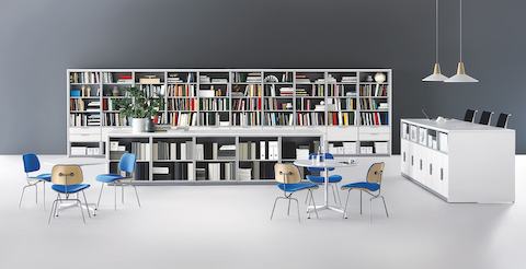 Blue-upholstered Eames Molded Plywood Chairs and white Eames Tables in a workplace library.