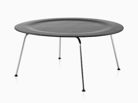 Una mesa de centro redonda de madera contrachapada moldeada Eames con patas de metal y una parte superior indentada en un acabado negro.