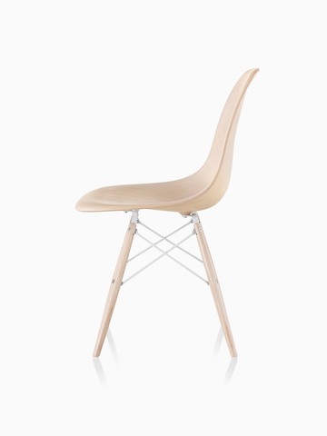 Vista de perfil de una silla lateral de madera moldeada Eames con un acabado ligero y patas de espiga.