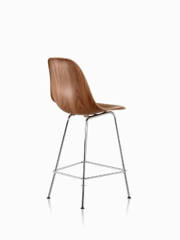 Three-quarter rear view of an Eames Molded Wood Stool with a medium finish and silver legs. 