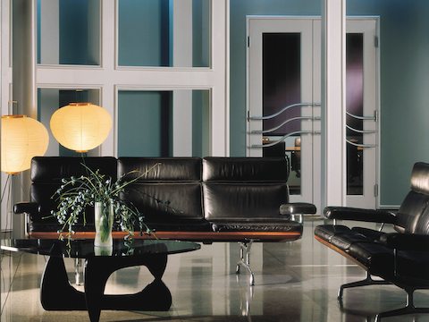Un sofá Eames de cuero negro, un loveseat Eames y una mesa Noguchi en el vestíbulo de una oficina.