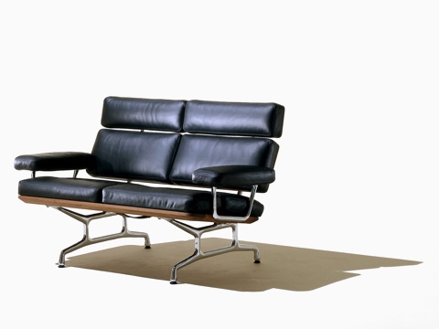 Oblique view of a black leather Eames loveseat with polished aluminum legs and arm supports.