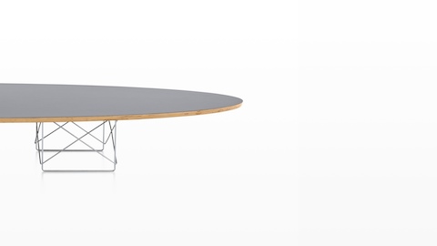 Una mesa elíptica de base de alambre Eames con una tapa gris en forma de tabla de surf.
