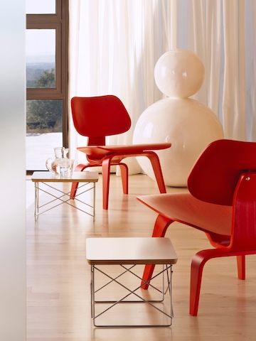 Dos tablas bajas con base de cables Eames combinadas con sillas de contrachapado moldeadas Eames de color rojo.