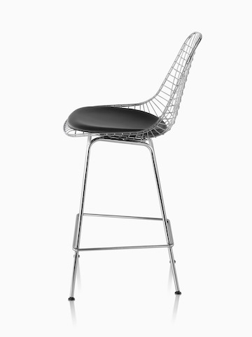 Profile view of a silver Eames Wire Stool with a black seat pad. 