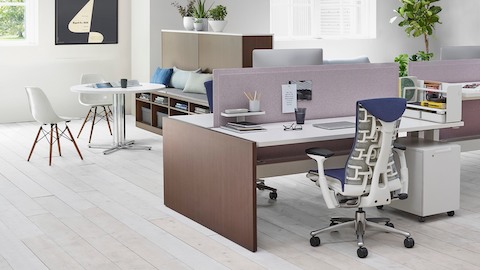 ブルーEmbodyオフィスチェア、ウッドベニアRenewリンクデスク、白いEames成形プラスチック製の椅子を示す作業設定。
