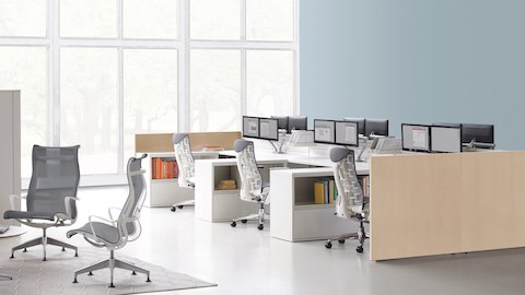 Gray upholstered Embody ergonomic desk chairs at Ethospace workstations with monitor arms in an open office near a lounge with Setu Lounge Chairs.