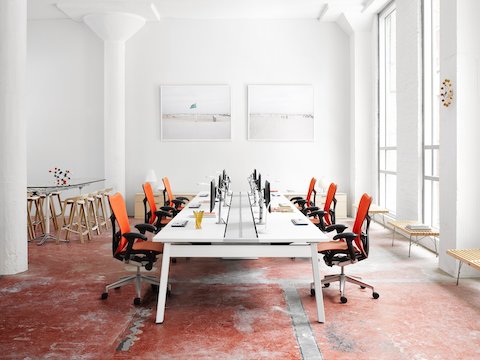 Orange Mirra 2 office chairs line either side of a Canvas Beam-based work surface with attached Flo Monitor Arms.