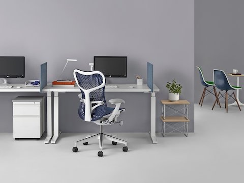 An individual work point featuring a blue Mirra 2 office chair, Renew Sit-to-Stand Table, and Flo Monitor Arm.