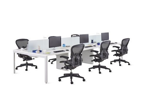 A white Layout Studio benching workstation for six with frosted glass center privacy screens, desk accessories, and six black Aeron Chairs.