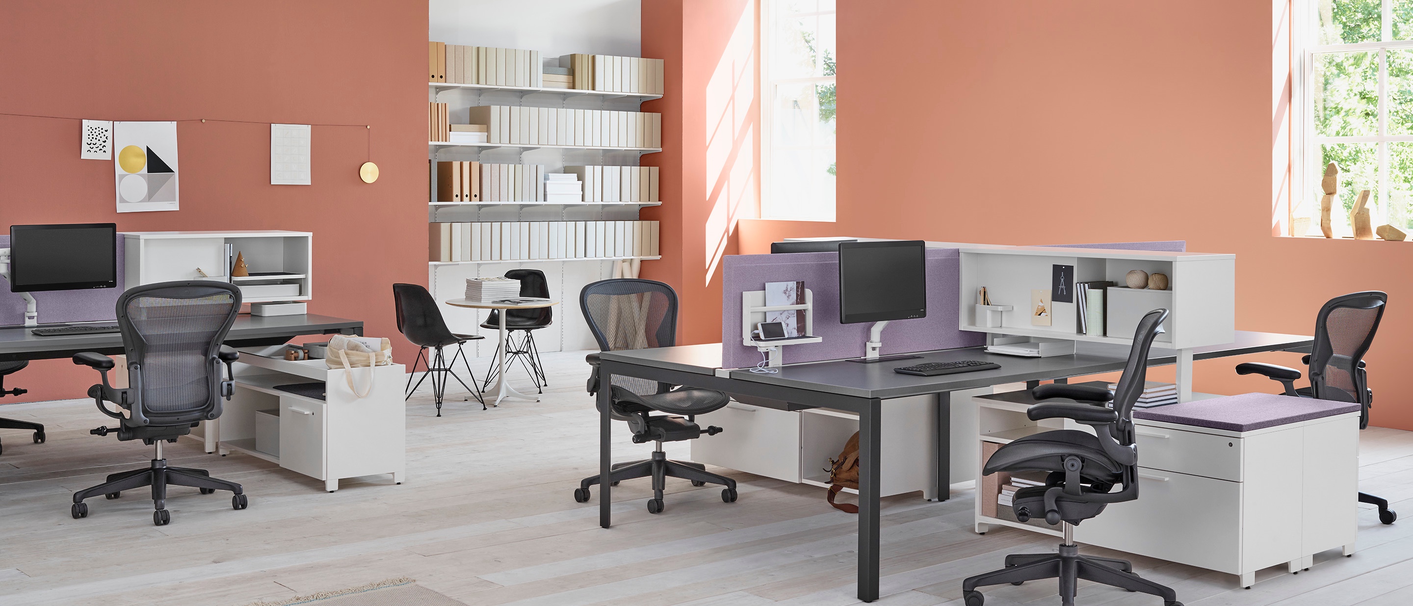 A workspace setting with two Layout Studio benches with purple fabric center privacy screens, Aeron Chairs, Tu Storage cubbies, and Tu credenzas.