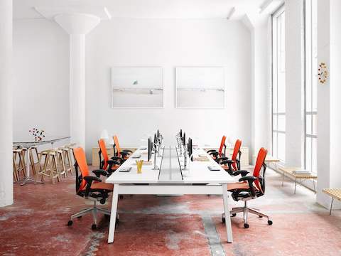 Un ambiente de trabajo brillante con sillas de oficina naranja Mirra 2 y otros taburetes y bancos.
