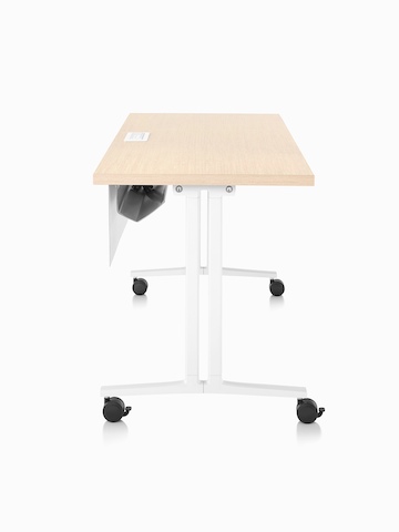 Side profile of a rectangular Everywhere Table with an ash woodgrain laminate top, white base with casters, and fabric modesty panel with cable trough.