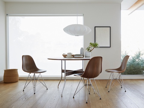 A Nelson Bubble Pendant lamp overhangs a Nelson Swag Leg Table surrounded by three Eames Molded Wood Chairs.