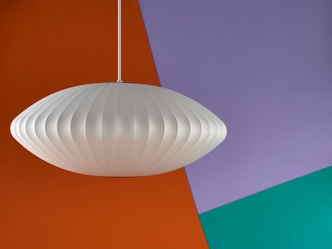 A Nelson Saucer Bubble Pendant lamp hanging in front of an orange, purple, and green background.