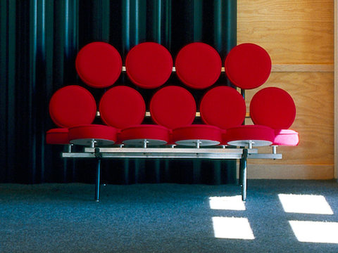 A Nelson Marshmallow Sofa upholstered in red fabric and situated in front of a blue curtain.