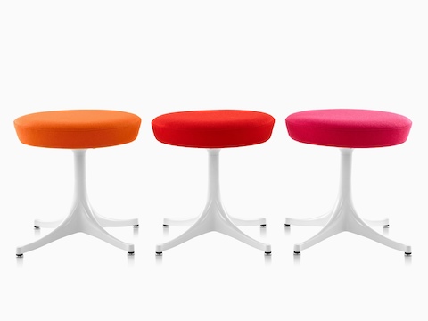 Three Nelson Pedestal Stools with orange, red, and pink upholstered seats and white bases.
